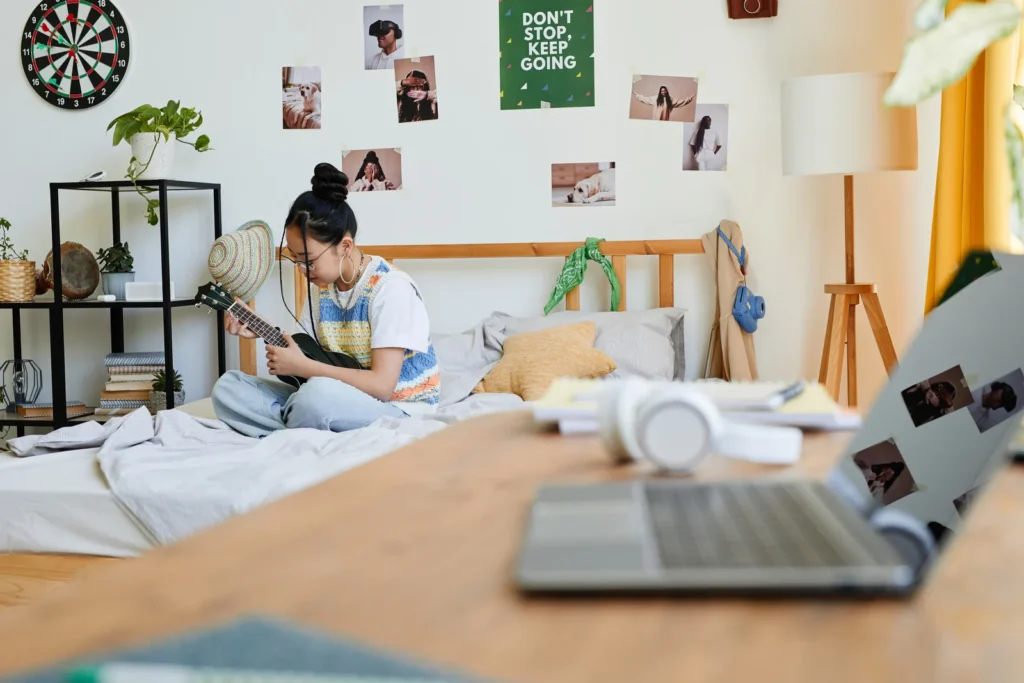 wall decor on teen girl's bedroom wall, photographs, dartboard, posters, teen girl sitting on her bed playing a guitar